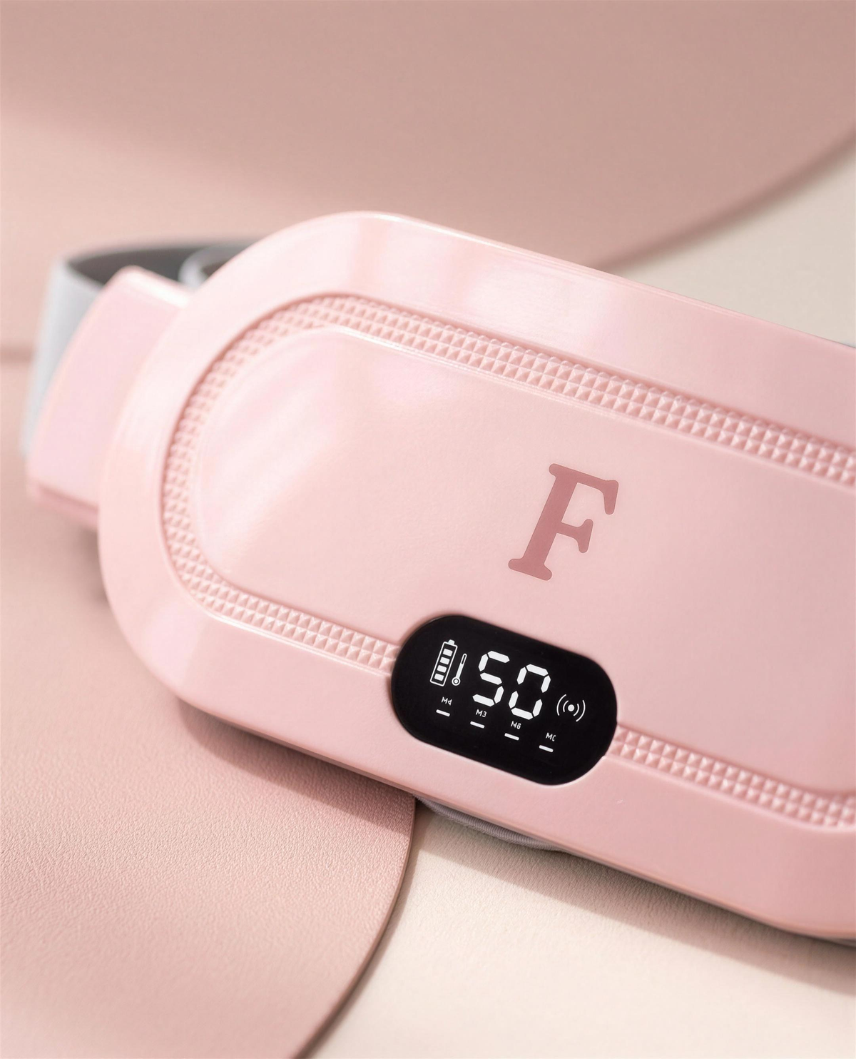 Gros plan sur le boîtier rose de la ceinture chauffante Feutrée : monogramme F, bord texturé et écran